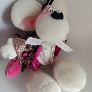 Könnte beinhalten: Ein Plüschtier, das eine Maus mit großen weißen Ohren und einem rosa Gesicht darstellt. Die Maus trägt eine rosa-gold gemusterte Jacke mit einer weißen Fliege. Sie hat große weiße Füße und schwarze Antennen.