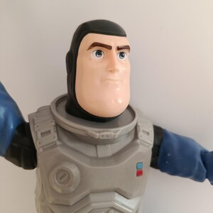 May include: A Buzz Lightyear action figure, featuring a light skin tone, black hair, and blue eyes. The figure wears a gray and blue space suit with a chest plate and blue sleeves. The toy is a collectible item.