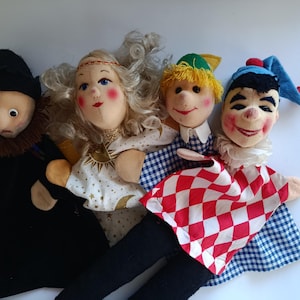 Op de afbeelding: Een set van vier stoffen handpoppen met een figuur in een zwarte mantel, een figuur met blond krullend haar in een witte jurk met hemelse patronen, een figuur met geel haar in een blauw geruit overhemd en een nar in een rood-wit ruitjespak.