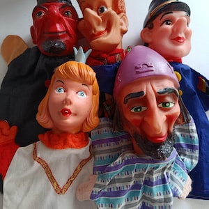 May include: A group of vintage hand puppets depicting different characters. The puppets include a red devil, a smiling man with orange hair, a police officer, a princess, and a bearded man with a purple hat. Each puppet has a distinct facial expression and costume.