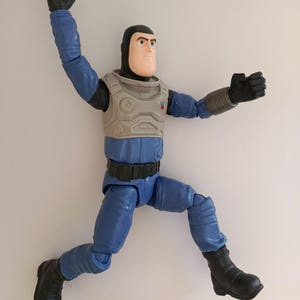 May include: A blue and gray action figure of a space ranger in a dynamic pose. The figure has a black helmet, gloves, and boots. The chest armor is gray, and the figure is posed as if jumping or flying.