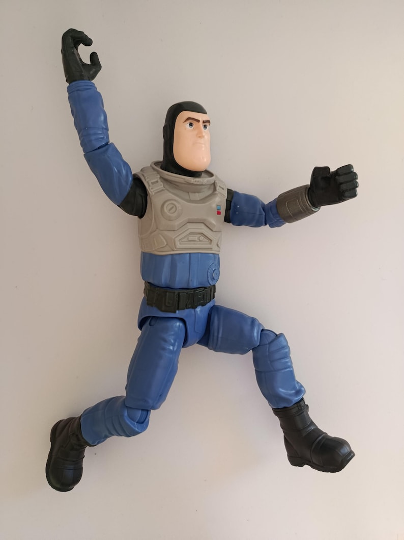 May include: A blue and gray action figure of a space ranger in a dynamic pose. The figure has a black helmet, gloves, and boots. The chest armor is gray, and the figure is posed as if jumping or flying.