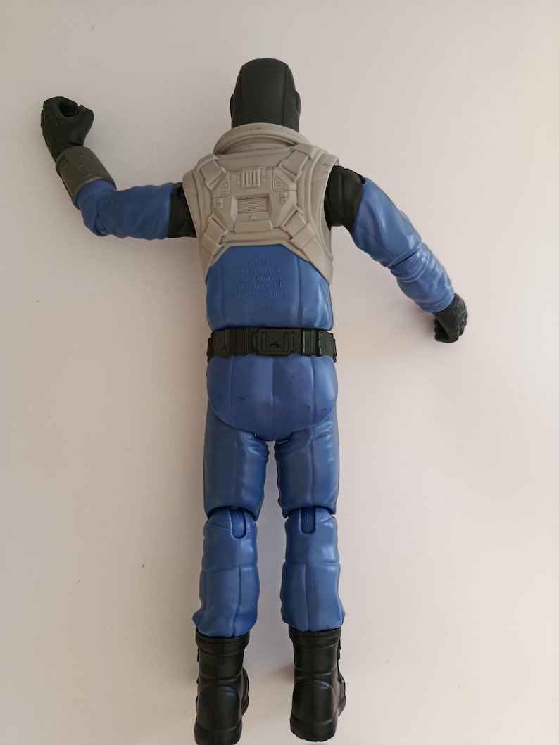 May include: A blue action figure of a character in a futuristic outfit. The figure has a black helmet, gloves, and boots. It wears a gray vest and a black belt. The figure's arms are outstretched, and it is posed against a white background.