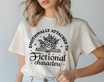 May include: Cream-coloured t-shirt with the text "Emotionally Attached to Fictional Characters." The design features an open book with flowers and stars. The text and graphic are in black.