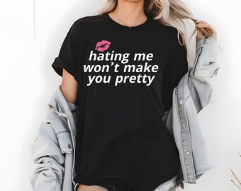 May include: Black t-shirt with the text "hating me won't make you pretty" in white, and a pink lip graphic. The shirt is a casual style, suitable for everyday wear.