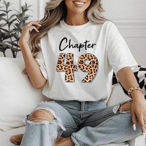 May include: White t-shirt with the text "Chapter 49" printed on it. The number 49 is printed in a leopard print pattern.