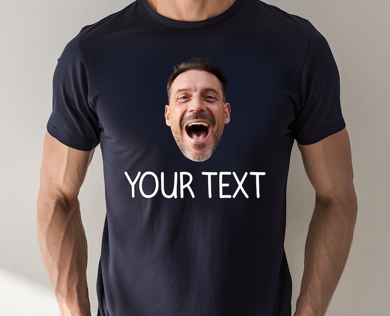 May include: Navy blue t-shirt with a printed image of a laughing man's face. The text "YOUR TEXT" is printed in white below the image. The shirt has short sleeves and a crew neck.