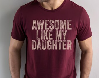 May include: Burgundy crew neck t-shirt with the text "AWESOME LIKE MY DAUGHTER" in distressed white lettering. The shirt is made of a soft material and is suitable for casual wear.