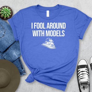 May include: A blue t-shirt with white text that reads "I fool around with models" and a white silhouette of a train engine.