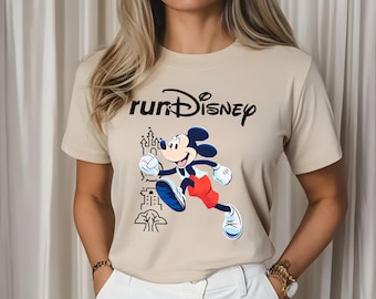 May include: Beige t-shirt featuring the text "runDisney" above a graphic of Mickey Mouse running. Mickey is wearing red shorts, blue shoes, and white gloves. A castle and tree are also in the graphic.