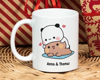 May include: White ceramic mug with a cartoon illustration of two bears hugging. The text "Anna & Thomas" is printed on the bottom of the mug.