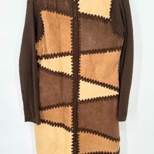 May include: A long, hooded coat with a patchwork design in shades of brown and tan. The coat features a full zipper and ribbed knit sleeves. The patchwork is sewn together with a decorative, scalloped stitch.
