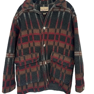 Puede incluir: Chaqueta de lana a cuadros en tonos marrón, rojo, gris y negro. La chaqueta tiene cuello, dos bolsillos delanteros y cierre de botones. La etiqueta dice "Woolrich".