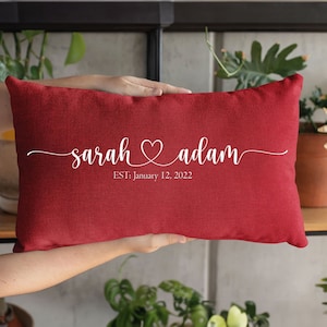 Peut inclure: Un coussin rouge avec du texte blanc qui dit "sarah ♥ adam EST: January 12, 2022".