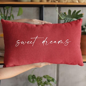 Könnte beinhalten: Rotes Kissen mit weißem, kursivem Text, der "sweet dreams" lautet.