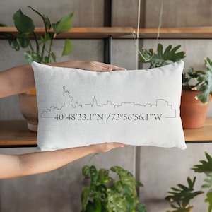 Puede incluir: Almohada blanca con un dibujo de línea negra del horizonte de la ciudad de Nueva York y las coordenadas "40°48'33.1"N / 73°56'56.1"W"