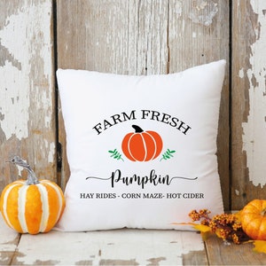 May include: White throw pillow with the text "FARM FRESH Pumpkin HAY RIDES - CORN MAZE - HOT CIDER" and a graphic of an orange pumpkin with green leaves.