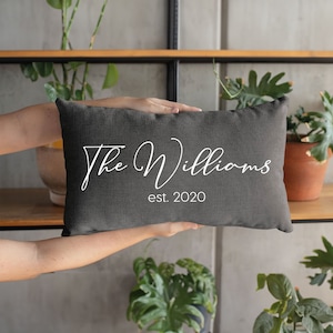 May include: A grey throw pillow with white text that reads "The Williams est. 2020".