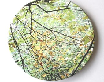 Round ceramic coaster with green tree branch print.