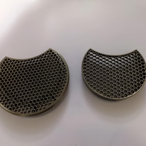 May include: Two metallic, crescent-shaped objects with a honeycomb pattern. The objects are a dark, muted gold color and have a rounded edge. The larger object is slightly thicker than the smaller one, and both are set against a white background.
