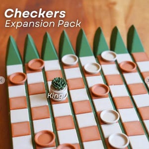 K&ouml;nnte beinhalten: Ein Checkers-Erweiterungspack mit einem Holzbrett mit einem Gitter aus wei&szlig;en und orangefarbenen Quadraten. Das Brett hat gr&uuml;ne dreieckige Akzente. Die Spielsteine sind Terrakotta- und wei&szlig;e Scheiben. Eine kleine Sukkulentenpflanze in einem wei&szlig;en Topf befindet sich in der Mitte des Bretts, mit dem Wort "King" auf dem Topf.