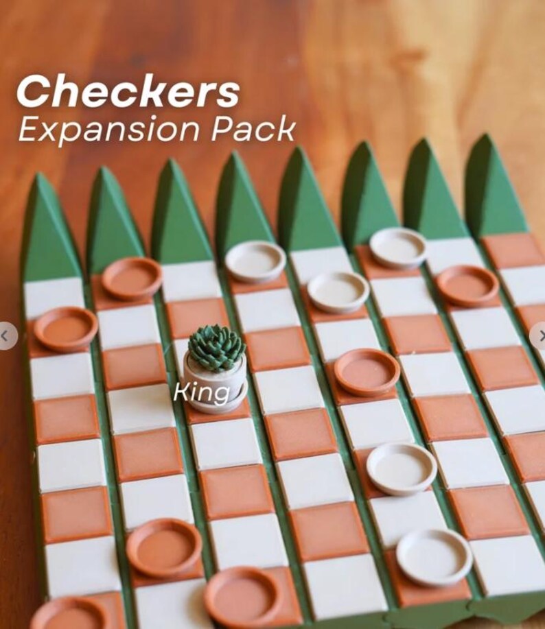 K&ouml;nnte beinhalten: Ein Checkers-Erweiterungspack mit einem Holzbrett mit einem Gitter aus wei&szlig;en und orangefarbenen Quadraten. Das Brett hat gr&uuml;ne dreieckige Akzente. Die Spielsteine sind Terrakotta- und wei&szlig;e Scheiben. Eine kleine Sukkulentenpflanze in einem wei&szlig;en Topf befindet sich in der Mitte des Bretts, mit dem Wort "King" auf dem Topf.