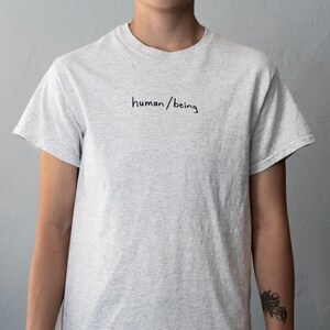 May include: A gray t-shirt with the text "human/being" written in black ink on the front.