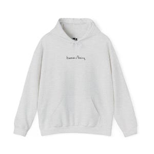 May include: A heather grey hooded sweatshirt with a kangaroo pocket and the text "human/being" embroidered on the front.