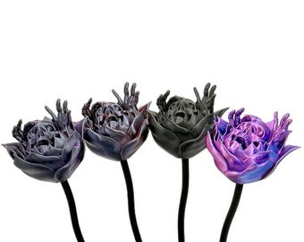May include: Four decorative flower sculptures with a unique design. Each flower features a skull-like face and outstretched hands, with colors ranging from dark purple to black and iridescent purple. The stems are black.