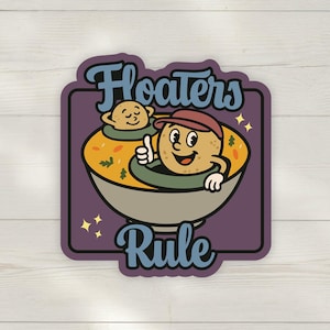 Peut inclure: Autocollant avec une illustration de dessin animé d'une pomme de terre dans un bol de soupe, faisant un signe de pouce. Un autre personnage flotte dans la soupe. Le texte "Floaters Rule" est au-dessus et en dessous.