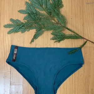 May include: Teal blue underwear with a small brown tag that says "Made in USA" and "Eco-Friendly"