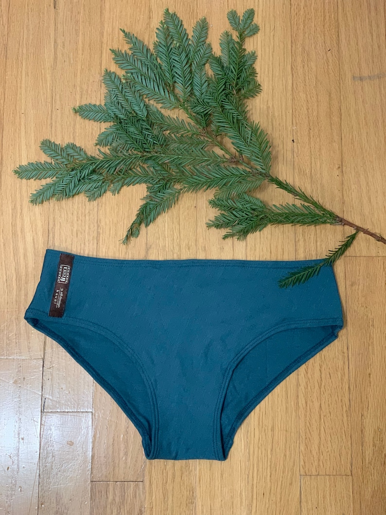 May include: Teal blue underwear with a small brown tag that says "Made in USA" and "Eco-Friendly"