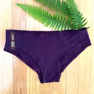 May include: Purple underwear with a brown tag that says "Made in USA" and "soft design".