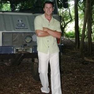 Puede incluir: Un hombre con una camisa de manga corta verde claro y pantalones blancos est&aacute; de pie frente a un cami&oacute;n grande de color gris. El cami&oacute;n tiene una parrilla negra y un parachoques negro. El hombre sonr&iacute;e y mira a la c&aacute;mara.
