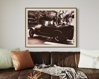 May include: A brown leather sofa with throw pillows and a blanket, a coffee table with a book and a glass, and a vintage black and white photo of a car on the wall.