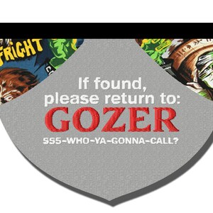 May include: A gray, heart-shaped tag with a white border and black text. The tag has a white background with a black border and the text "If found, please return to: GOZER 555-WHO-YA-GONNA-CALL?" in white. The tag is decorated with a colorful, cartoon-style image of a monster.