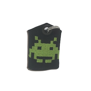 May include: Black key chain with a green pixelated alien design.