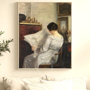 May include: A framed vintage painting shows a woman in a light dress reading a newspaper. The artwork has a muted colour palette and soft lighting. The painting is displayed in a room with other framed art and decorative objects.