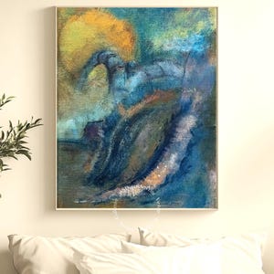 May include: Abstract art print with a gold frame. The artwork features a blend of blues, greens, and yellows, with brushstrokes creating a textured effect. The painting is mounted above a bed with white pillows.