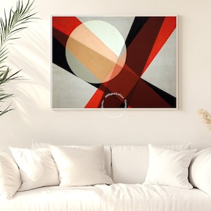 May include: Abstract geometric art print featuring a white circle and intersecting shapes in red, black, and beige against a gray background. The artwork is framed and displayed above a white sofa, creating a modern interior design.