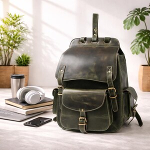 Può includere: Uno zaino in pelle verde oliva scuro caratterizzato da una grande patta principale con due cinghie con fibbia verticali, una tasca frontale con chiusura a fibbia singola e due tasche laterali. La borsa presenta cuciture e fibbie in ottone.