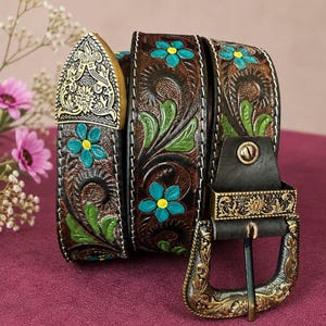May include: A dark brown leather belt featuring intricate floral tooling with hand-painted turquoise flowers, yellow centres, and green leaves. The belt includes an ornate, antiqued brass-tone metal buckle and a matching decorative metal tip.