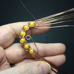 May include: A copper wire wrapped around a row of yellow beads, forming a crescent shape.