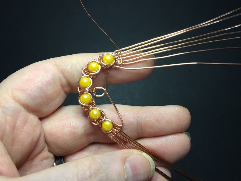 May include: A copper wire wrapped around a row of yellow beads, forming a crescent shape.