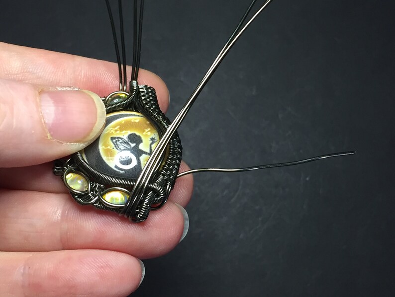 May include: A close-up of a wire-wrapped pendant featuring a round cameo with a fairy silhouette and the text "then to the..." The pendant is accented with iridescent beads and has multiple wires extending from the back.