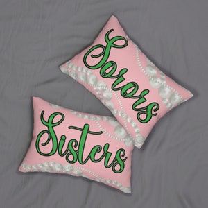 Op de afbeelding: Twee roze kussens met witte parel-achtige ontwerpen en groene tekst. Een kussen zegt "Sorors" en de andere zegt "Sisters".