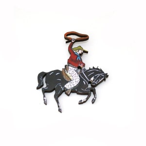 May include: A wooden cutout of a cowboy riding a black horse. The cowboy is wearing a red shirt, white pants, a green hat, and is holding a lasso.
