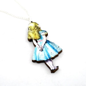 May include: A wooden pendant necklace featuring a painted image of Alice from Alice in Wonderland. Alice is wearing a blue dress and has blonde hair. The pendant is attached to a silver chain.