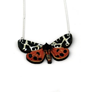 May include: A silver chain necklace with a wooden pendant shaped like a butterfly. The butterfly is painted with black, white, red, and orange colors.