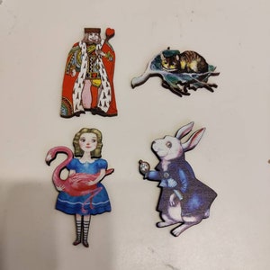 May include: Four wooden Alice in Wonderland character ornaments. The ornaments feature the King of Hearts, Alice holding a flamingo, the White Rabbit, and the Cheshire Cat.